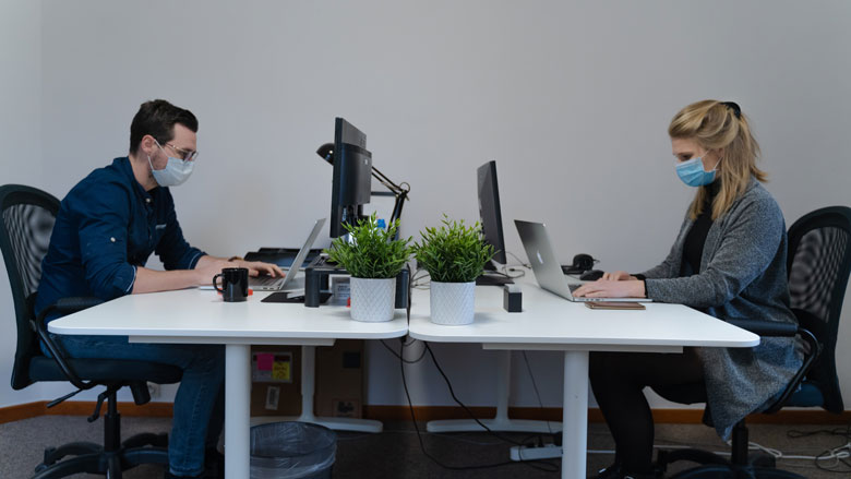 Zwei Personen, die in einem Büro an ihren Computern arbeiten und Masken tragen